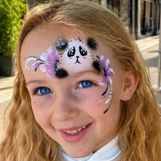 A smiling child with a panda and lilac flowers painted on their forehead